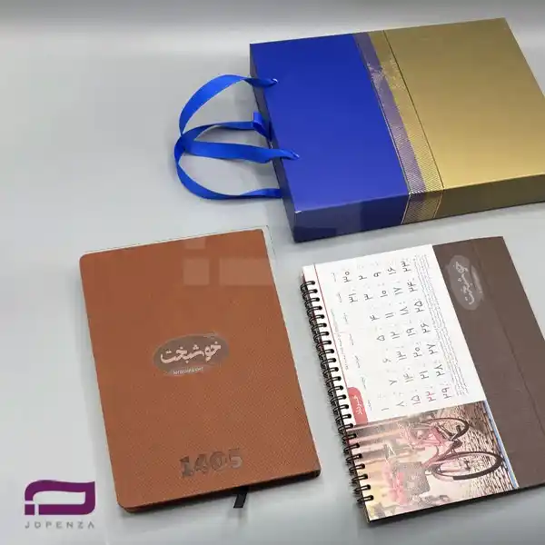 ست سالنامه تقویم رومیزی P974 شامل سررسید رقعی روزانه و تقویم رومیزی جهانگردی با جلد سلفونی قهوه ای + ساک دستی لوکس طلایی آبی